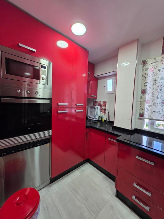 a red kitchen with red cabinets and a microwave at Magnífico alojamiento cerca de Mezquita catedral in Córdoba