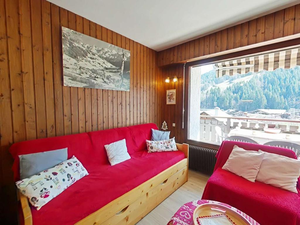 - un canapé rouge dans une chambre avec une grande fenêtre dans l'établissement Studio 4 pers, centre village, proche commerces et pistes, TV incluse - FR-1-241-29, au Grand-Bornand