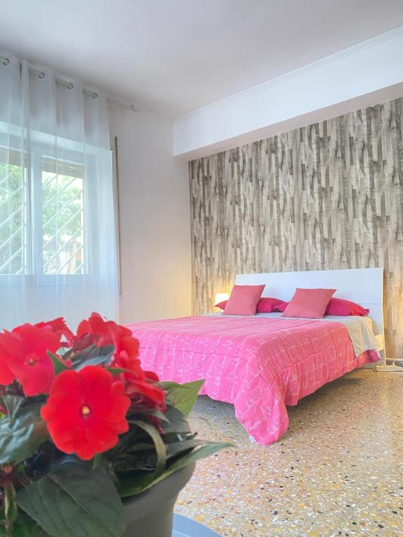 a bedroom with a pink bed and a vase of red flowers at Casa Linda in Lido di Ostia