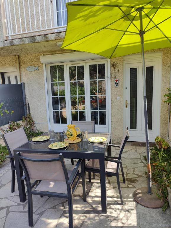 une table et des chaises noires avec un parapluie jaune dans l'établissement Maison Côté Plage Grau d'agde, au Grau-dʼAgde