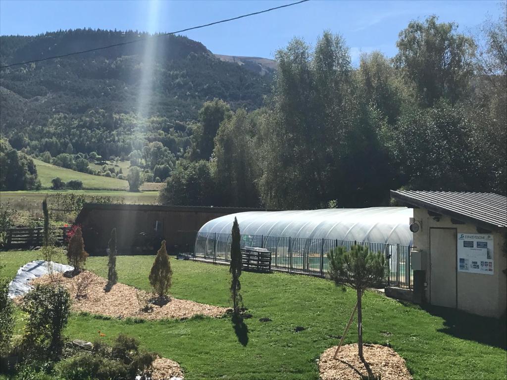 a building with a greenhouse in a field with trees at Le Relais de la Forge in Selonnet