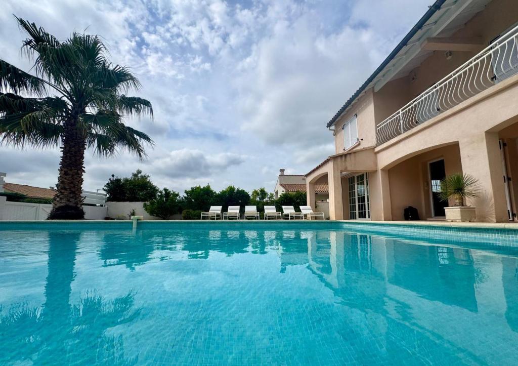 a large swimming pool next to a building with a palm tree at La Villa verdoyante in Baillargues