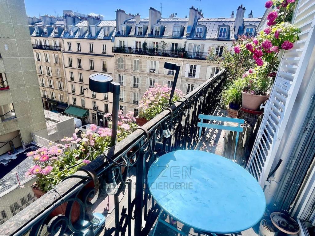 une table bleue sur un balcon avec des fleurs et des bâtiments dans l'établissement Au pied de la promenade Pereire - Paris 17, à Paris