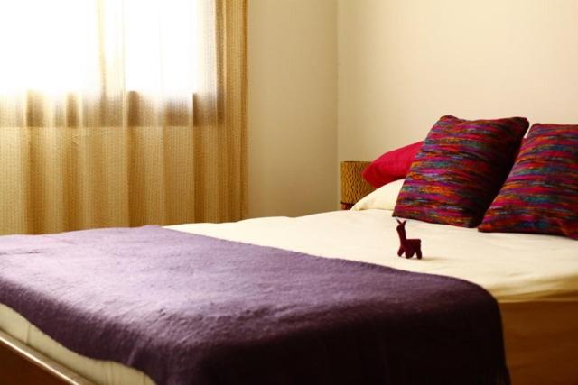 un gato sentado en una cama con una manta púrpura en Casa Suyay en Tilcara