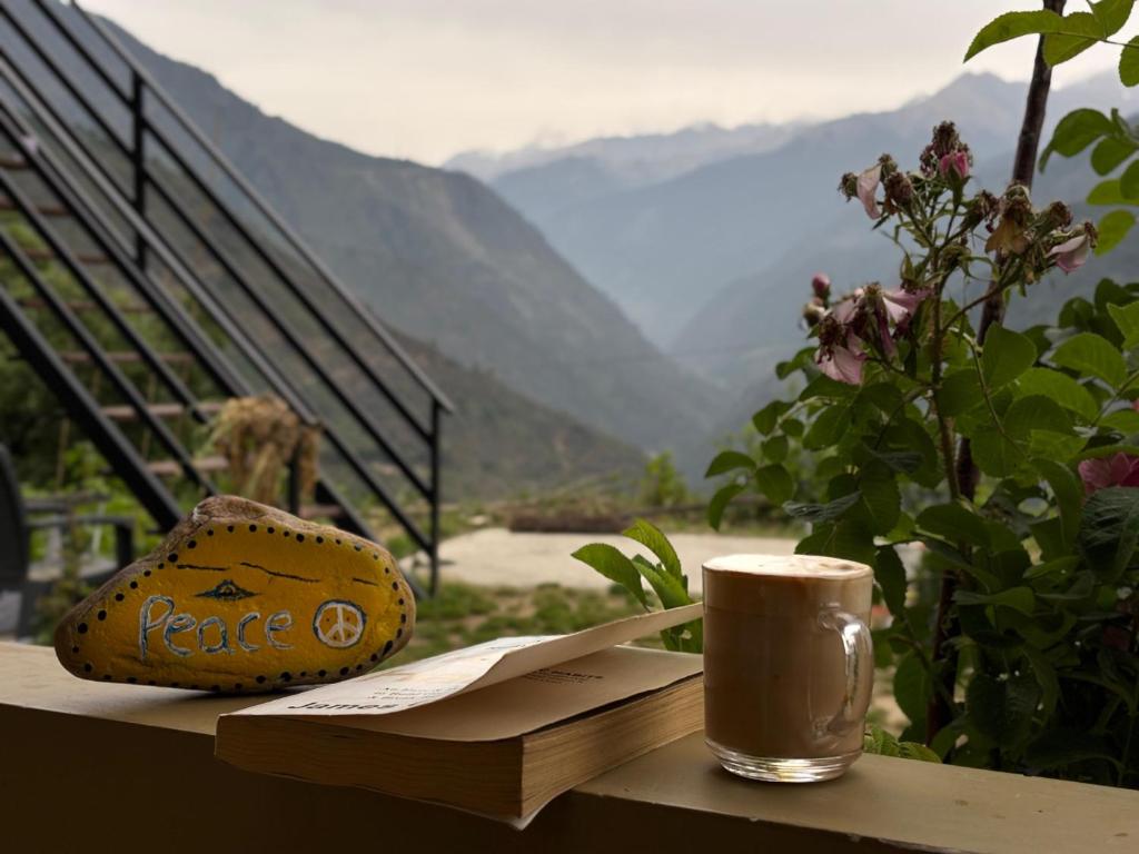 a coffee cup sitting on a table with a view of mountains at Gaonvasi Homestay in Uttarkāshi