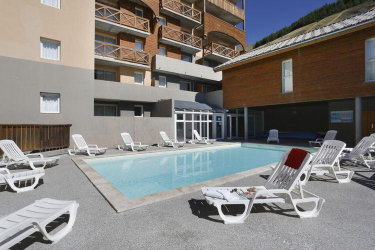une piscine avec des chaises longues à côté d'un bâtiment dans l'établissement Appartement 35 m2 4p avec piscine chauffée la foux d Allos, à La Foux d'Allos
