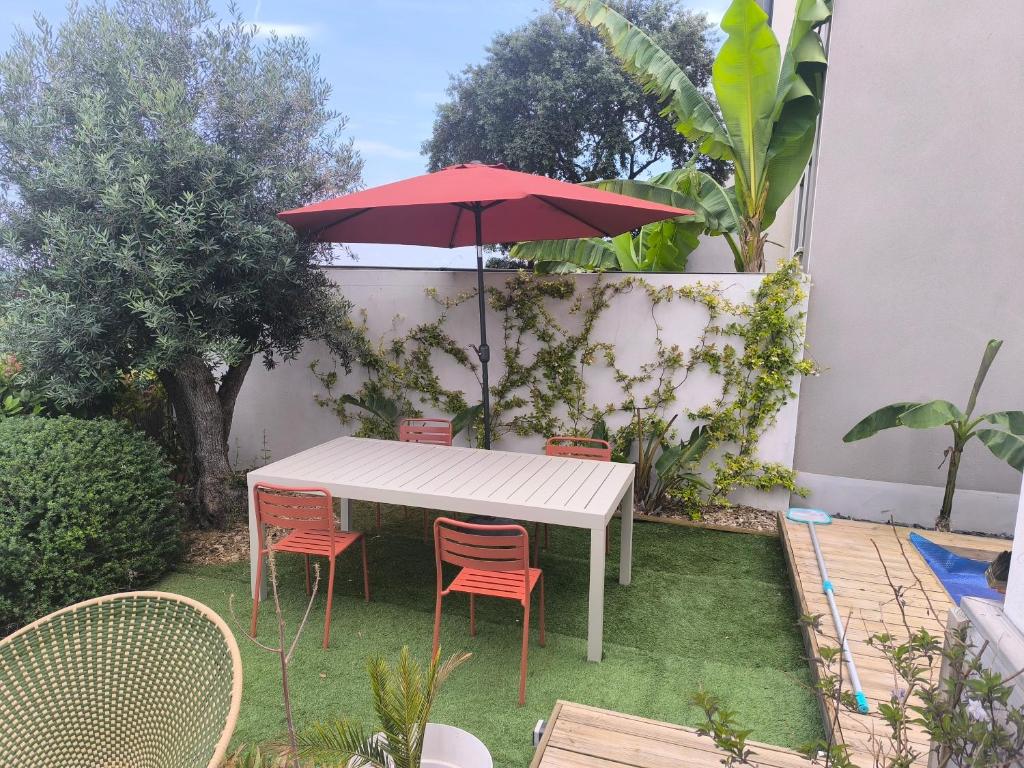 une table et des chaises blanches avec un parapluie rouge dans l'établissement Villa vacances Montpellier, à La Celle-sous-Gouzon