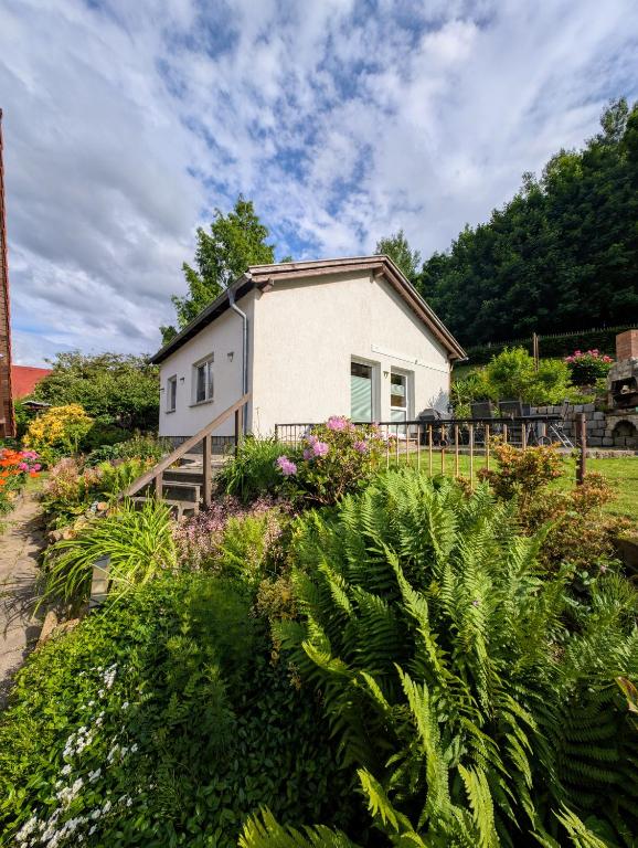 a small white house in a garden with flowers at Ferienhaus Marx in Sebnitz