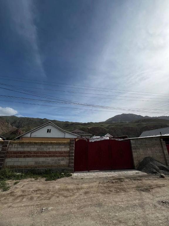 a red fence and a building with mountains in the background at Tian Shan Sky House in Naryn