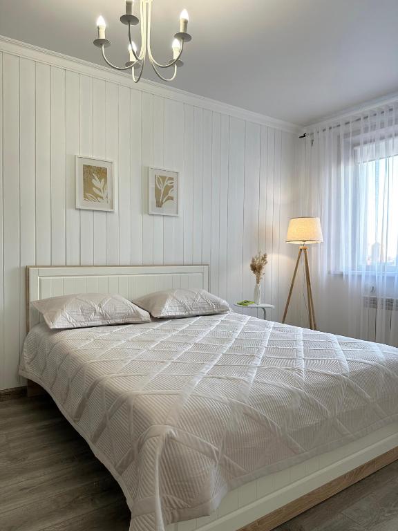 a white bed in a white bedroom with a chandelier at ЖК "Light House", 2 in Astana