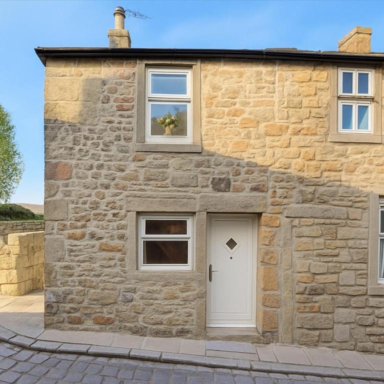 a stone house with a white door and two windows at Blossom Tree Cottage in Barnoldswick