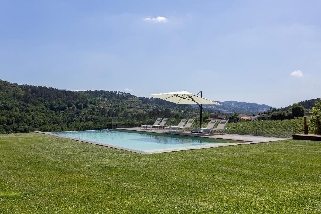 una piscina con sedie e un ombrellone su un campo erboso di Casa do Cipreste em Amarante 