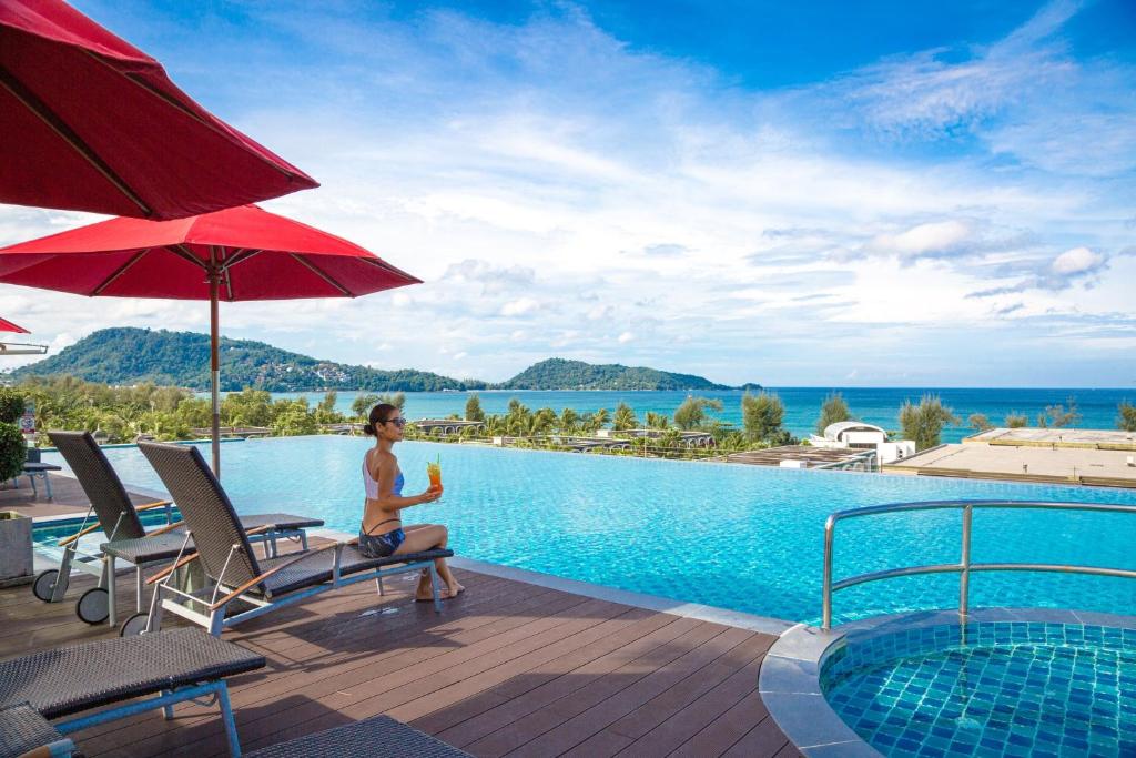 a man sitting on a chair next to a swimming pool at Beachfront and Deluxe Pool Access Patong Phuket in Patong Beach