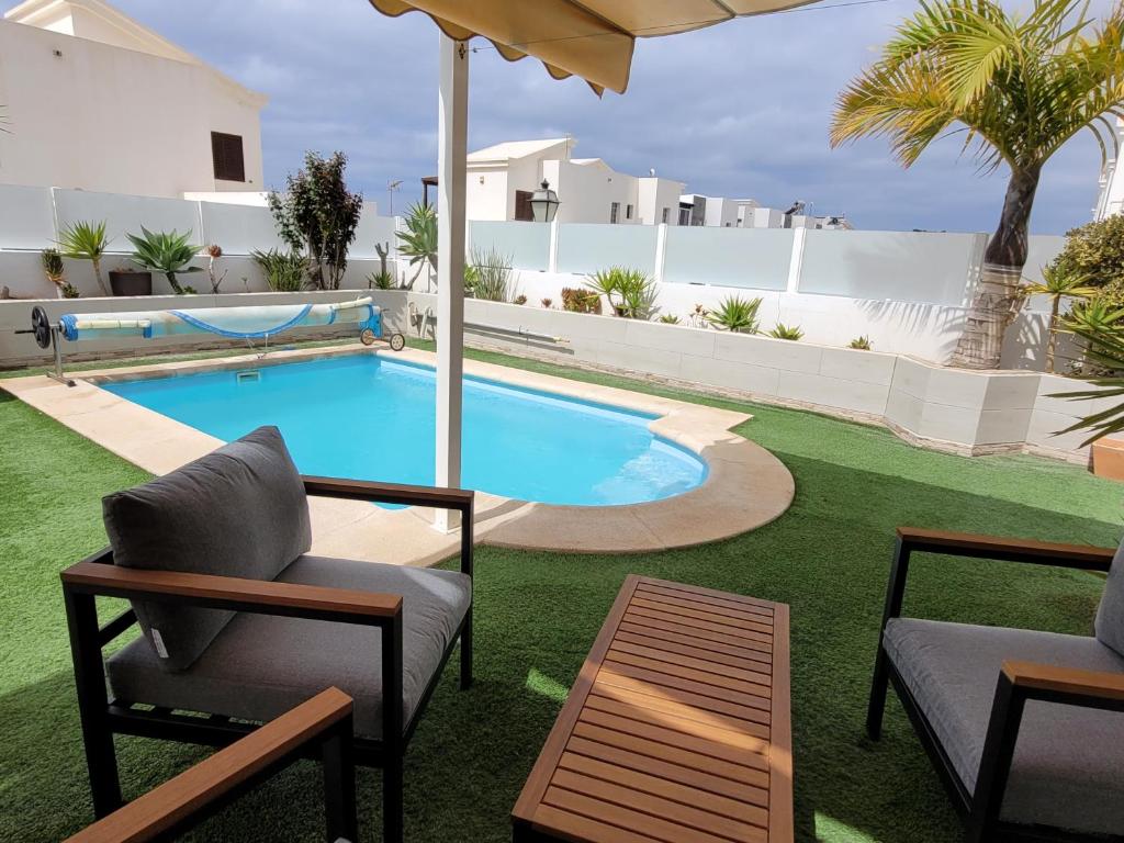 a swimming pool with chairs and an umbrella in a yard at Villa Vista with heated pool & Jacuzzi in Playa Blanca