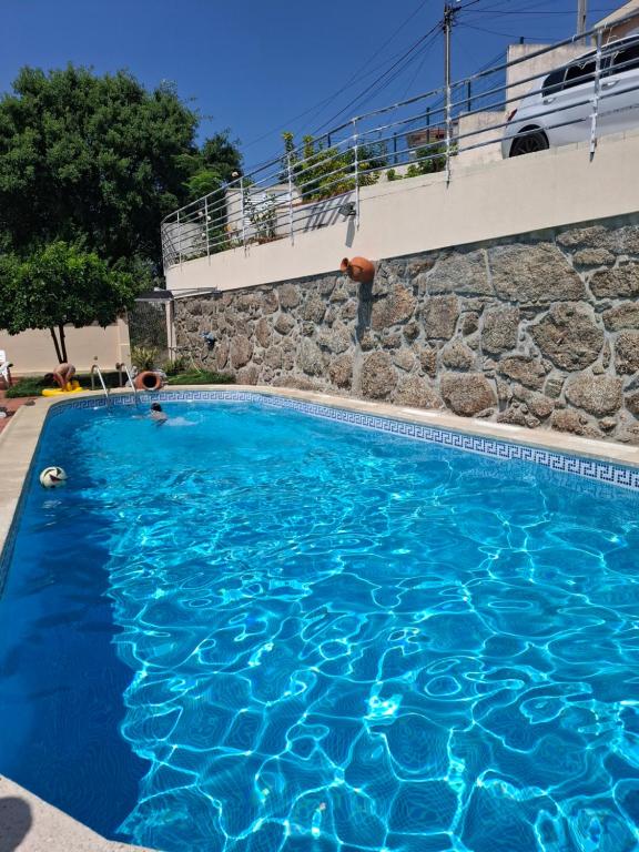 a swimming pool with blue water and a rock wall at Casa do Diniz in Travassos