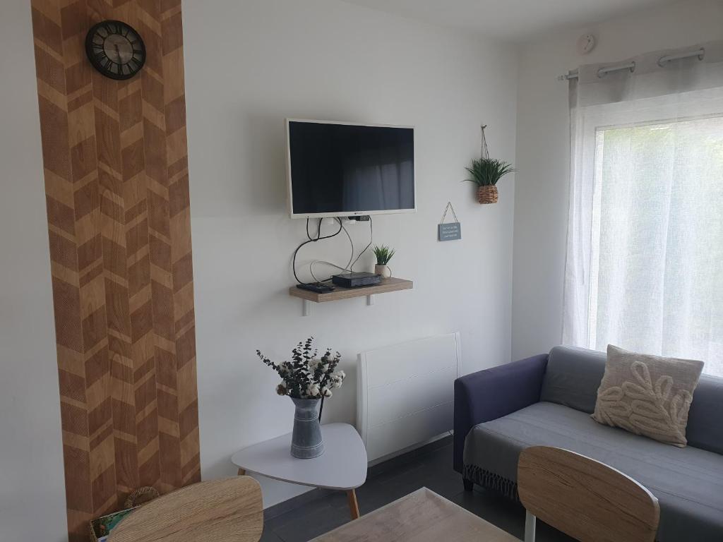 a living room with a couch and a tv on the wall at L'Echappée Verte - Guînes, maison 2 chambres à 25min du Site des 2 Caps in Guînes
