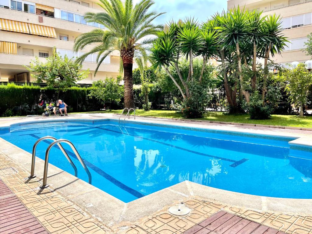 a swimming pool with palm trees and a building at APARTBEACH NARGAM Vista Playa in La Pineda