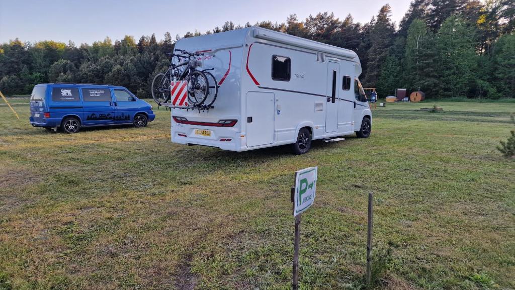 a white caravan parked in a field next to a blue van at SPK kempings in Laugaļi
