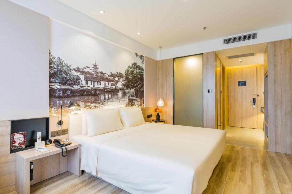 a bedroom with a large white bed and a painting on the wall at Atour Hotel (Suzhou Wujiang Fenxi) in Suzhou