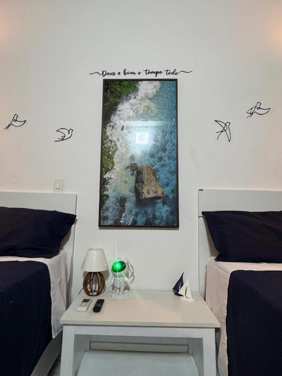 a bedroom with two beds and a table with a picture on the wall at suite ao som do mar - tombo guaruja in Guarujá