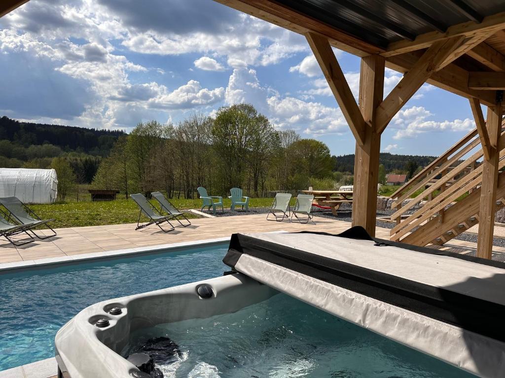 a swimming pool with a bed and chairs and a patio at Chalet PLUME D'EAU - jacuzzi, piscine et pétanque in Gerbépal