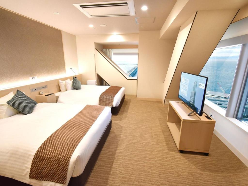a hotel room with two beds and a flat screen tv at Odysis Suites Osaka Airport Hotel in Izumi-Sano