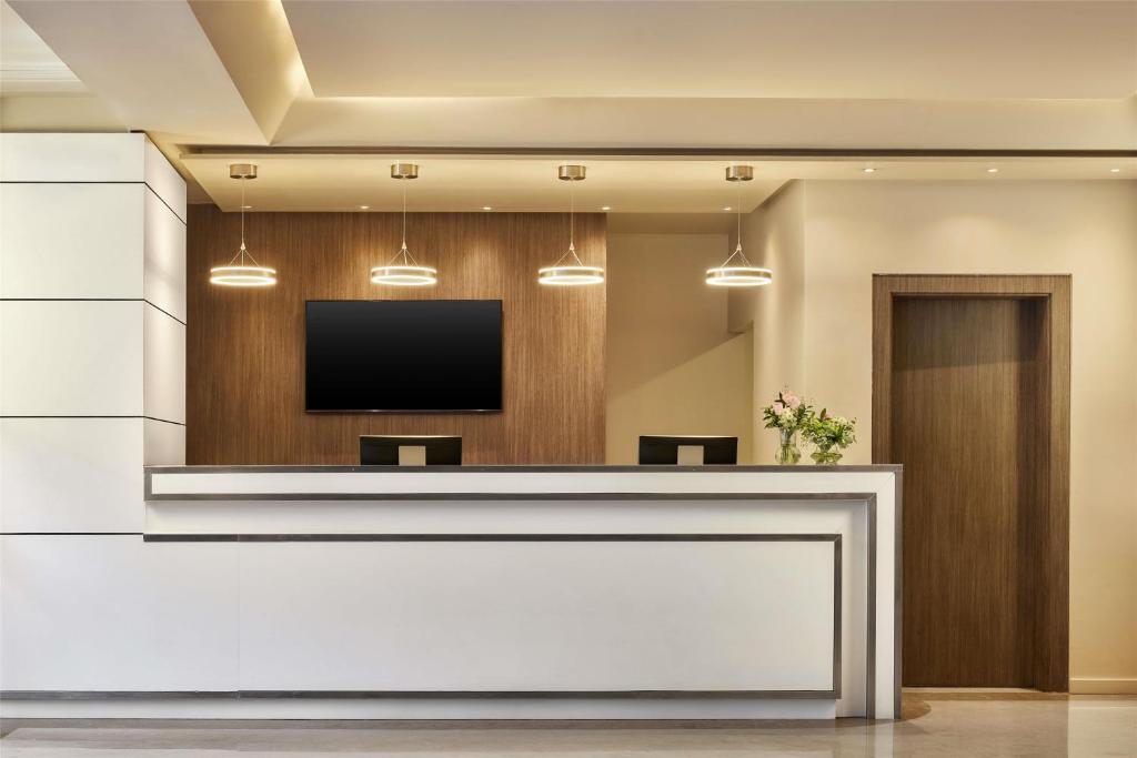 A streamlined reception desk sits beneath pendant lights and a wall-mounted television.