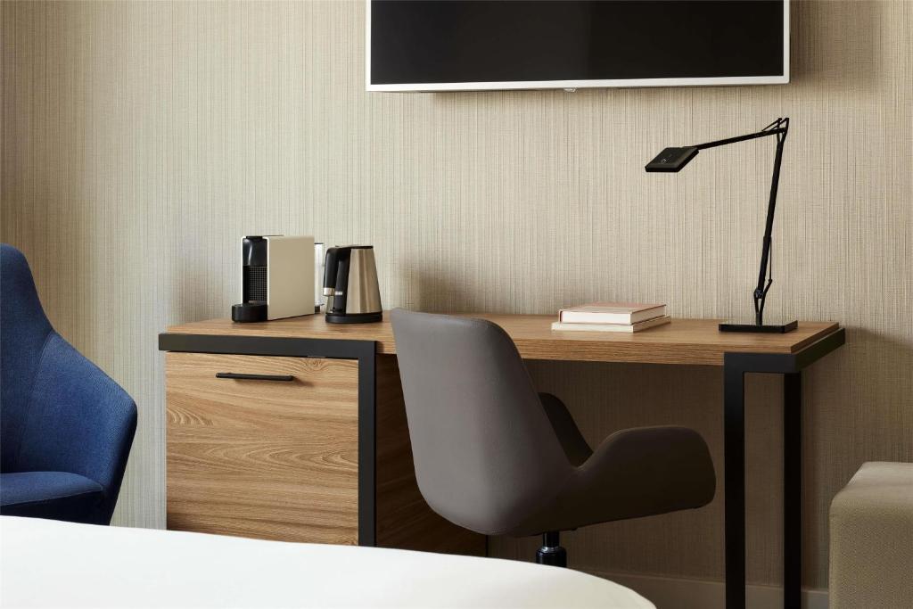 A compact hotel-room desk with a task lamp, chair, television and beverage station.