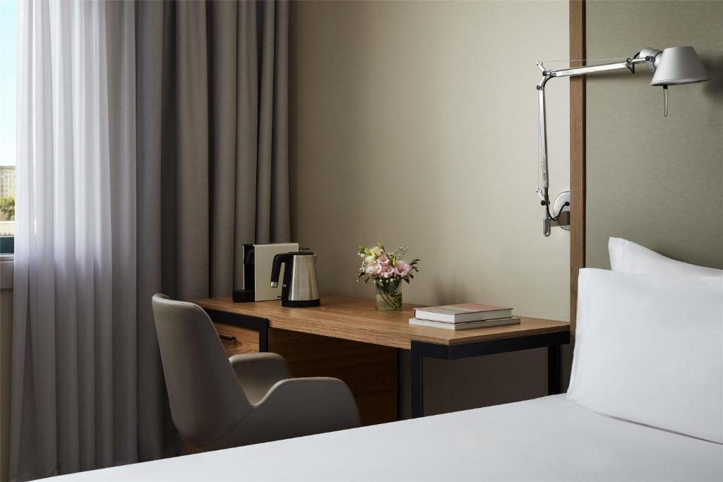 A single-bed room corner combining a bed, desk and curtained window.