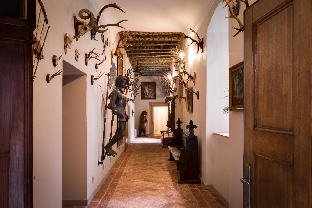 Antique hallway lined with mounted antlers, suits of armor, wooden benches, atmospheric dim lighting.