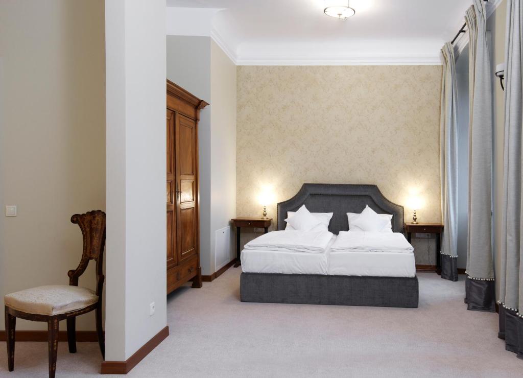 Spacious neutral bedroom with grey upholstered bed, wooden armoire, vintage chair and soft lighting