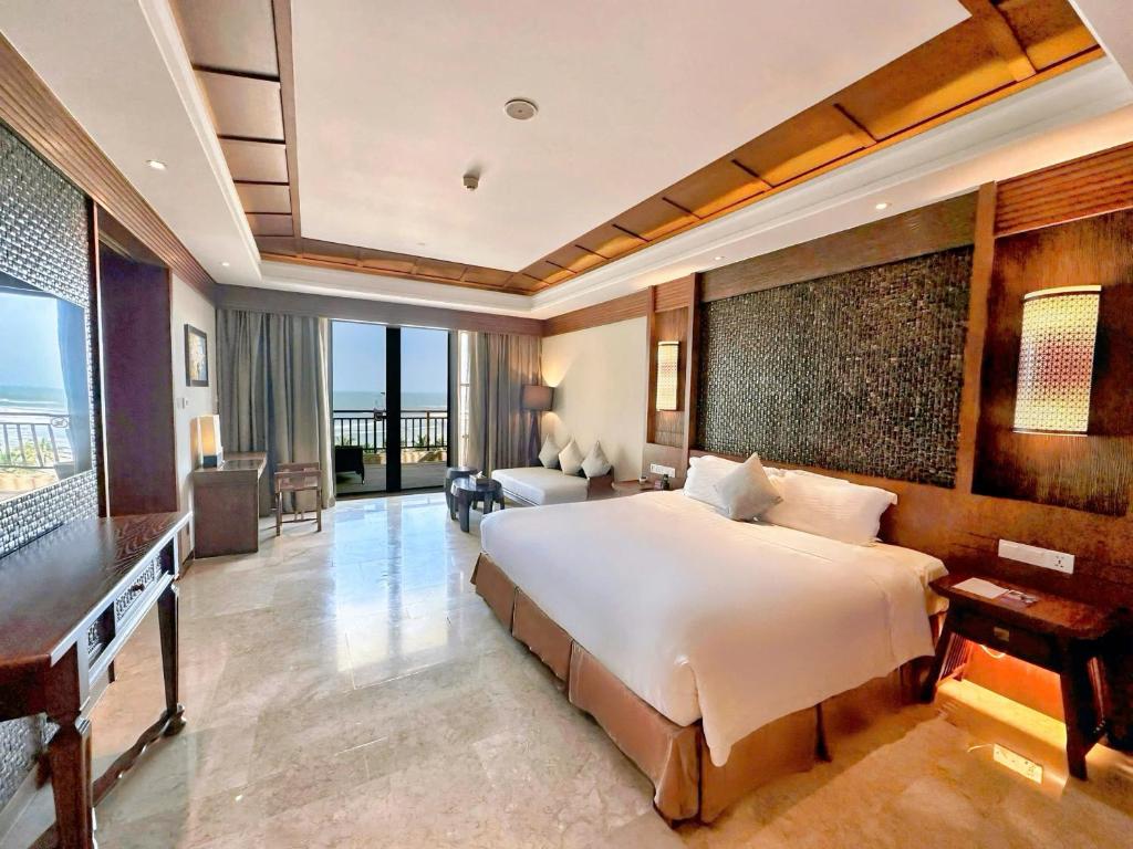 A large bedroom has a king-style bed, television, seating area and glazed opening toward a balcony or exterior view.