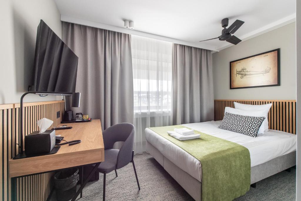 a hotel room with a bed and a desk and a tv at AIRINN Vilnius Airport Hotel RENOVATED 2025 in Vilnius