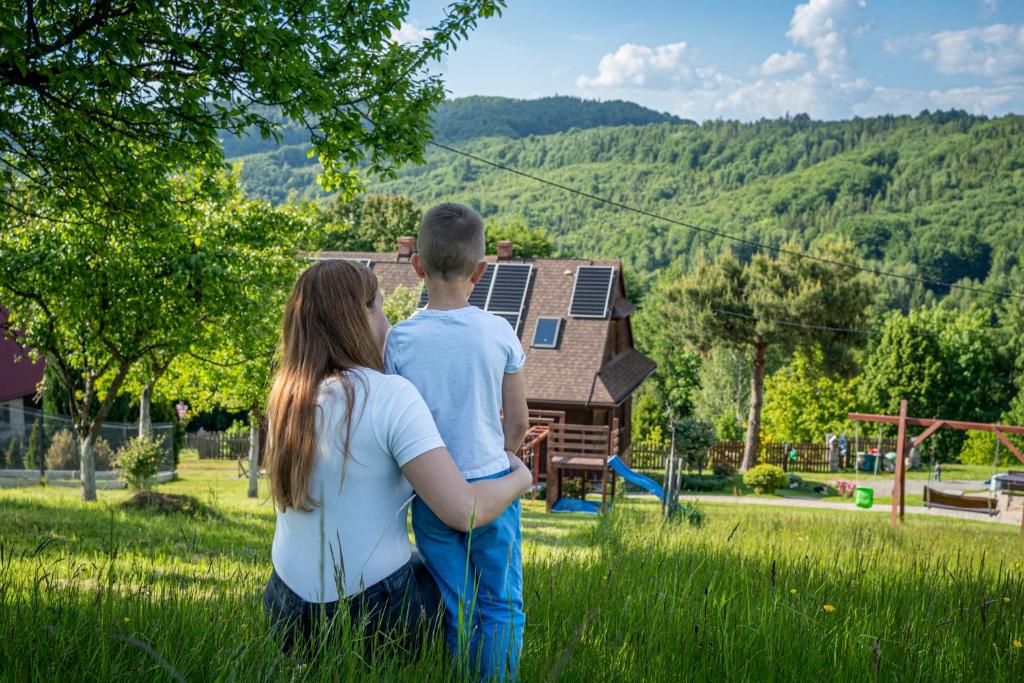 a boy and a girl standing in the grass with a house at Beskidzki Zakątek Ustroń - Przytulny domek z balią i kominkiem, idealny na relaks i ucieczkę od miasta in Ustroń