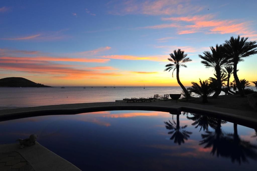 a pool with palm trees and the ocean at sunset at Villa Marlin by Cabo Villas in La Paz
