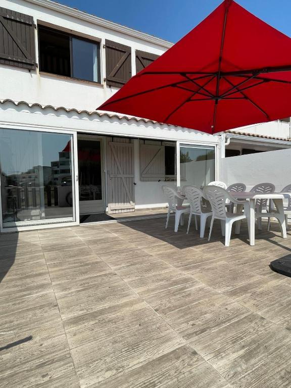 un patio avec une table, des chaises et un parasol rouge dans l'établissement Charmante maison de vacances proche plage Saint Hilaire de Riez, Vendée, à Saint-Hilaire-de-Riez