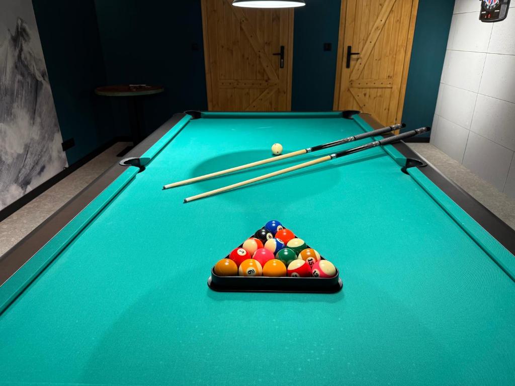 Billiards room featuring teal pool table, racked colorful balls and two cues, dim atmospheric lighting.