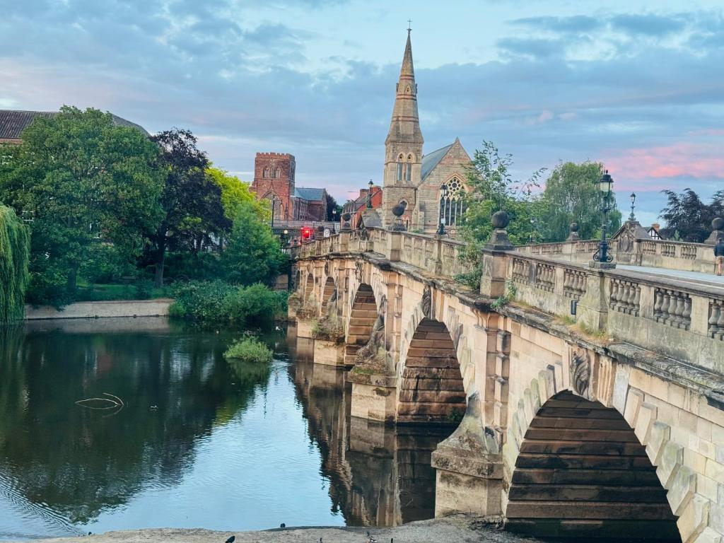 an old bridge over a river with a church at English Bridge Court in Shrewsbury