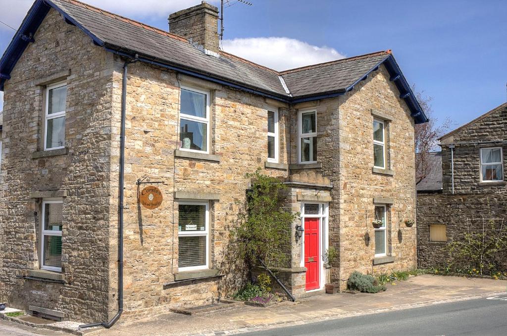 uma casa de tijolos com uma porta vermelha numa rua em Cornlee em Aysgarth