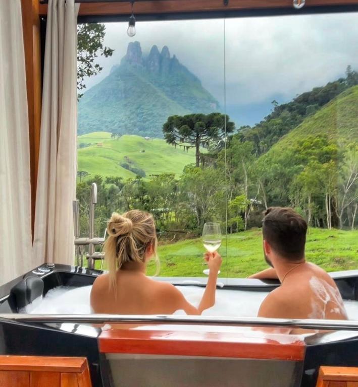 a couple sitting in a hot tub with a glass of wine at Cabana do Céu - Soldados Sebold in Alfredo Wagner
