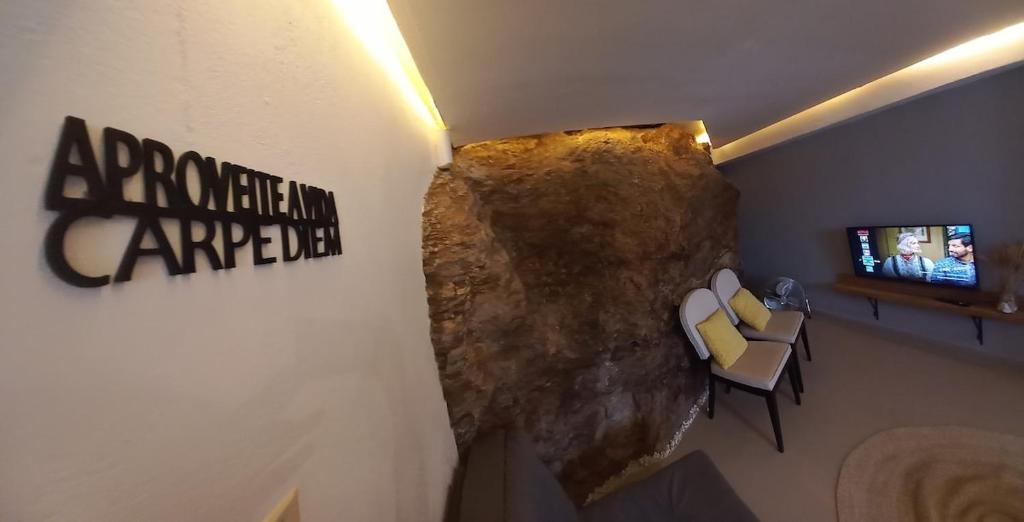 Una habitación con una pared de roca con un televisor y sillas. en 02 Lindo apartamento da pedra com churrasqueira, en São Sebastião