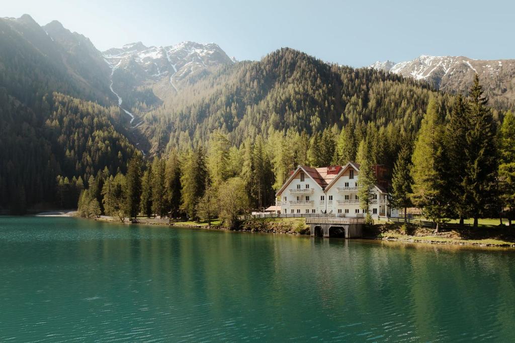 a large house on the edge of a lake with mountains at Antholzer Wildsee Haus in San Giuseppe in Anterselva
