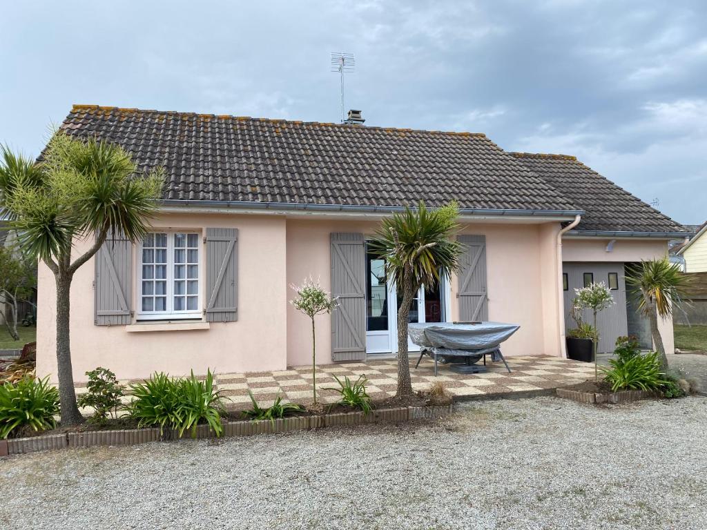 une maison rose avec des palmiers devant elle dans l'établissement Maison à 100 m de la plage, à Pirou