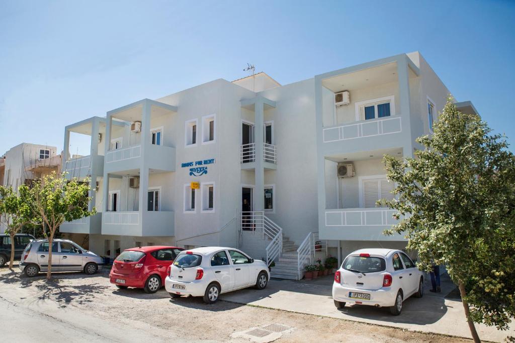 un edificio bianco con auto parcheggiate in un parcheggio di Revekka Rooms a Kíssamos