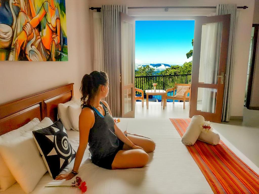 a woman sitting on a bed looking out the window at Grand Hills kandy in Kandy
