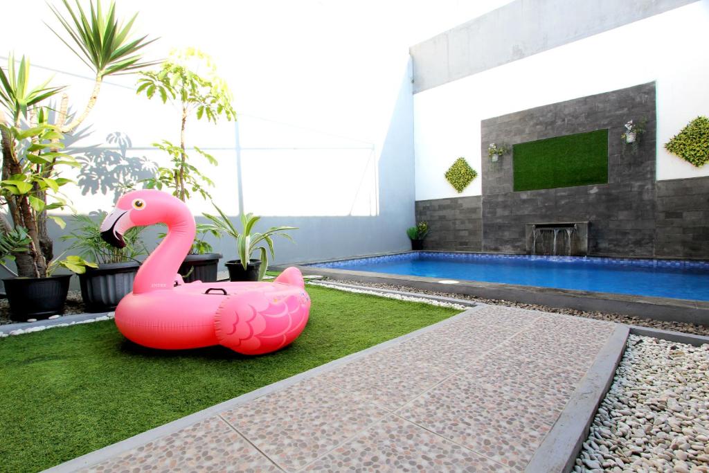 バンドンにあるVilla Normandieのピンク色のフラミンゴのぬいぐるみがプールの近くの芝生に座っている