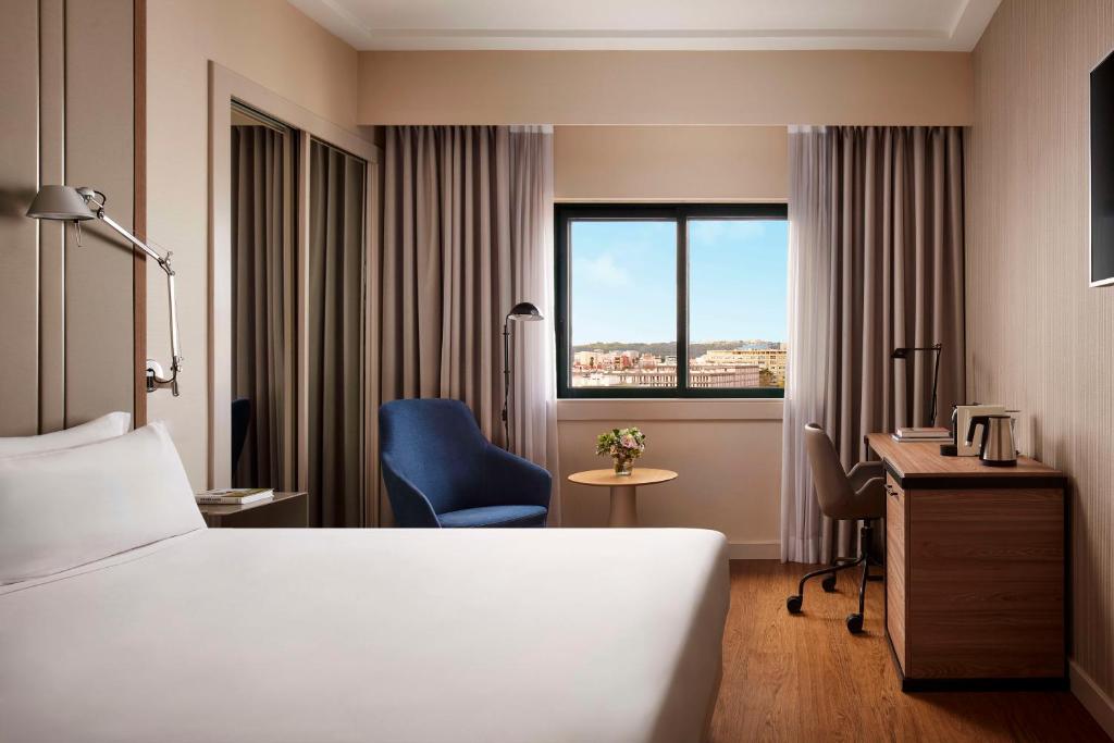 A compact room with a double bed, desk, armchair and a broad city view.