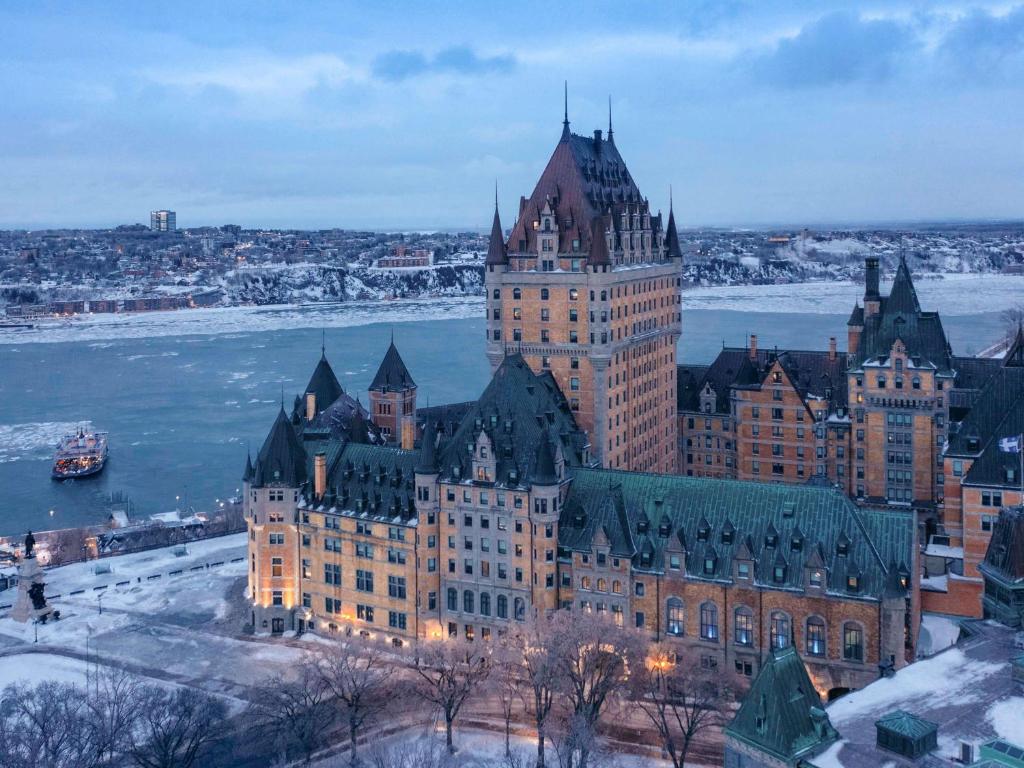 a large castle on the water in front of a city at Fairmont Le Chateau Frontenac in Quebec City