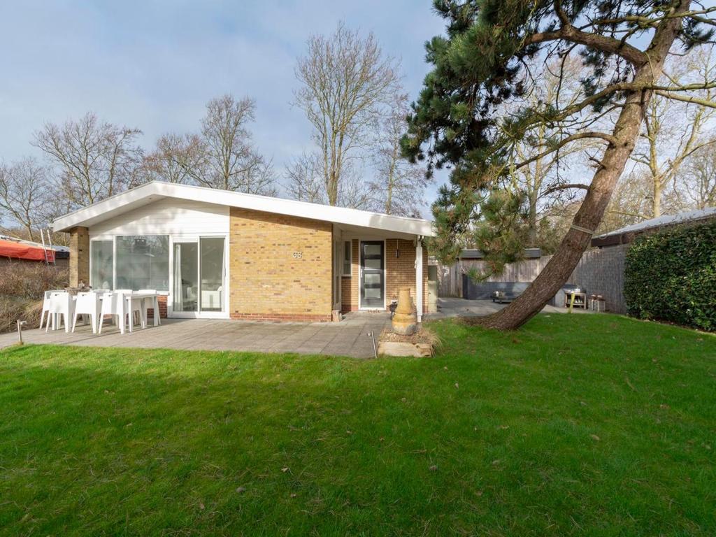 a small house with a patio and a tree at Bungalow in Sint Maartenszee near Beach in Sint Maartensvlotbrug