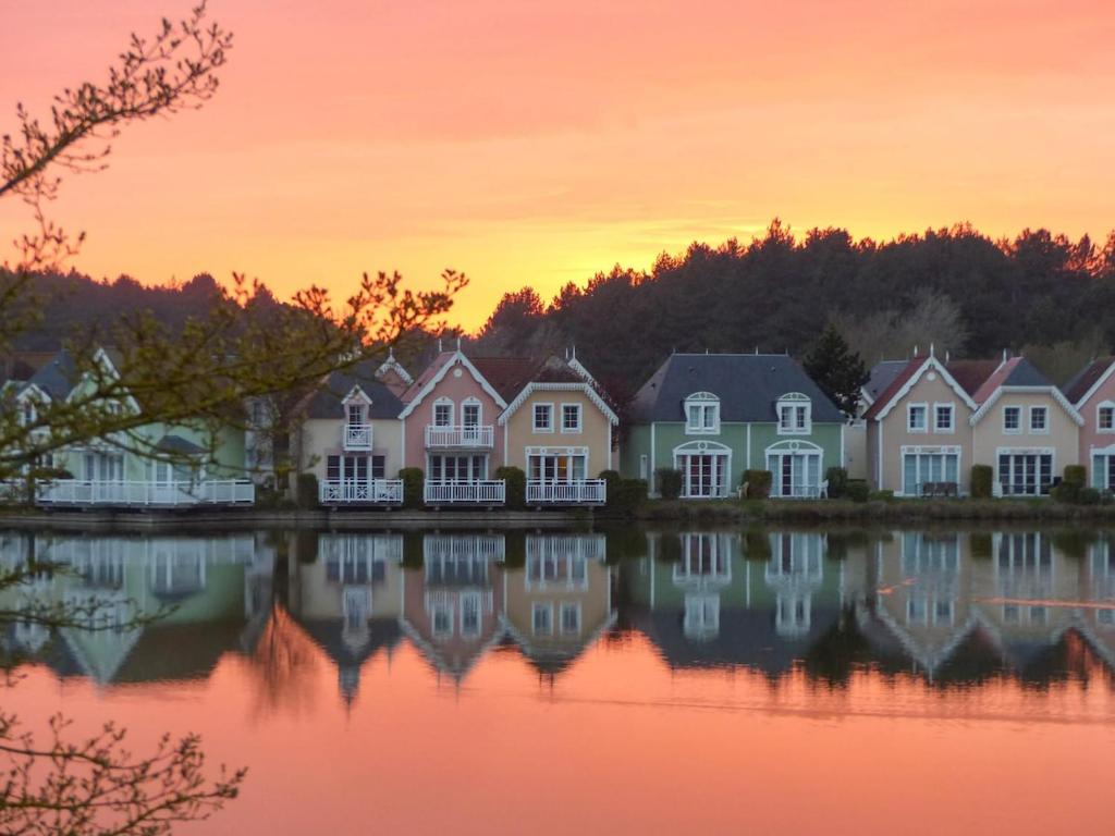 une rangée de maisons sur l'eau au coucher du soleil dans l'établissement Maison Fort Mahon Belle Dune Village Vacances, à Fort-Mahon-Plage